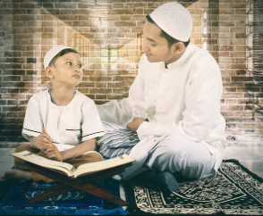 Comprehensive Quran Memorization FAQ for Parents A young boy and a man, both wearing white clothing and kufi caps, sit cross-legged on prayer rugs in front of an exposed brick wall. The boy holds a pencil over an open Quran on a wooden stand and looks up attentively at the man, who is gently guiding him during a study session.