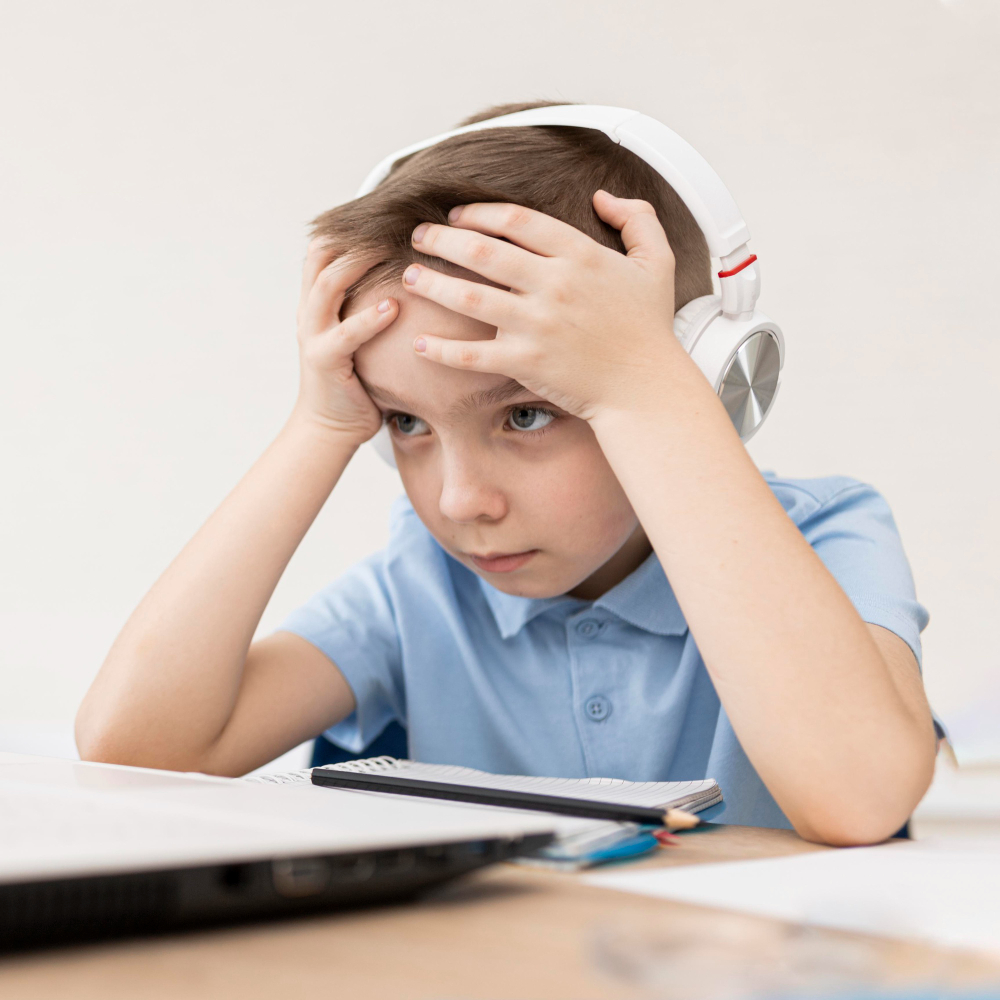 Solve Focus Before Blaming the Format A close-up photograph of a frustrated young boy wearing headphones and holding his head while looking at a laptop, a concept image showing the need to solve focus before blaming the format of online classes.