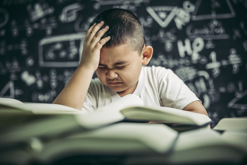 Why Kids Struggle to Stay Consistent with Quran Classes A detailed digital cartoon illustration of a tired young Muslim boy wearing a white t-shirt, resting his head heavily on his arm at a desk next to an open laptop and a green book, looking exhausted during a study session, capturing why kids struggle to stay consistent with quran classes.